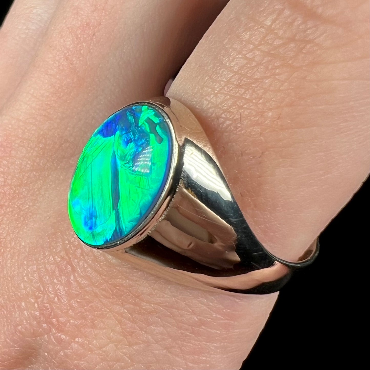 Close-up of 14k white gold Australian opal men's ring with green and blue flashes on finger