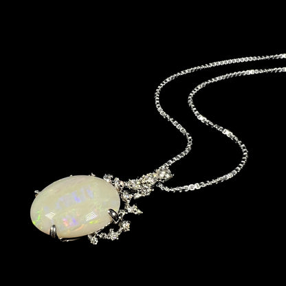 A white gold opal necklace lying at an angle on a black background, highlighting its intricate diamond design.