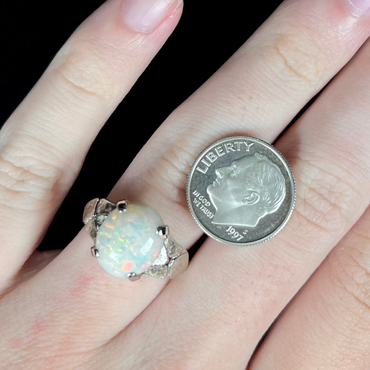 Close-up of hand wearing a white gold Australian opal solitaire ring next to a US dime coin