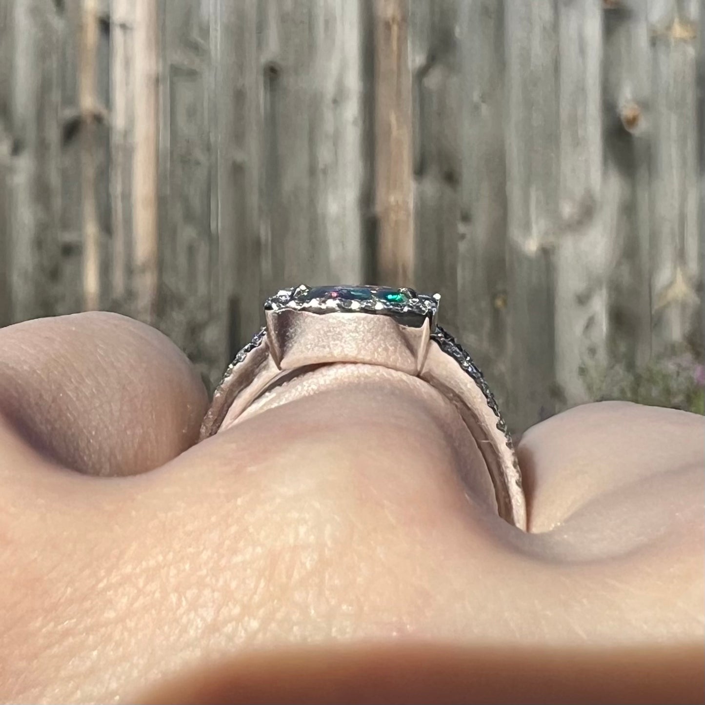 The gallery view of a white gold opal ring by artist Luciano Bortone, worn on a hand in daylight.