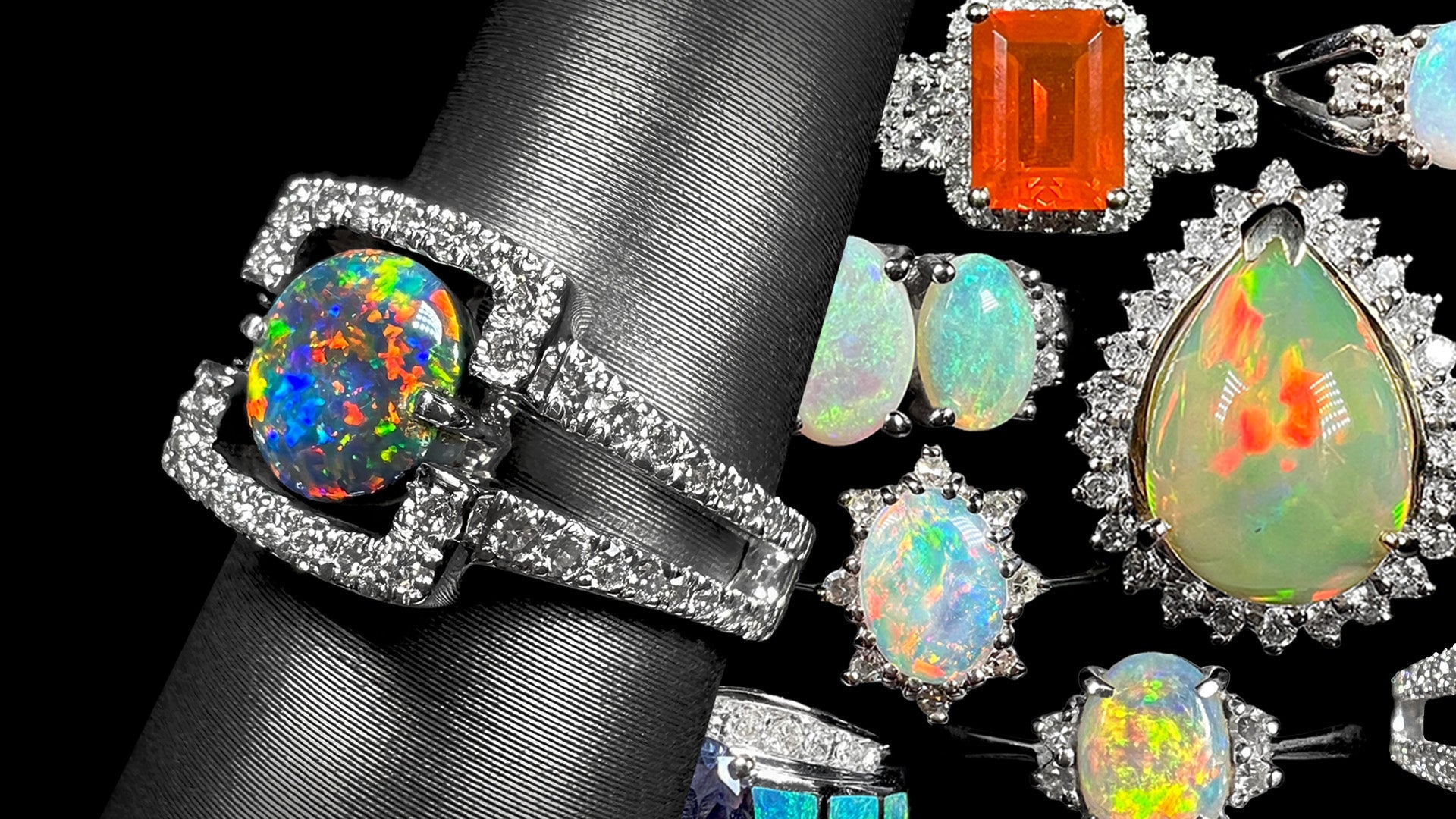 White gold black opal and diamond ring on ring display shown from angle in front of collection of colorful white gold opal rings.