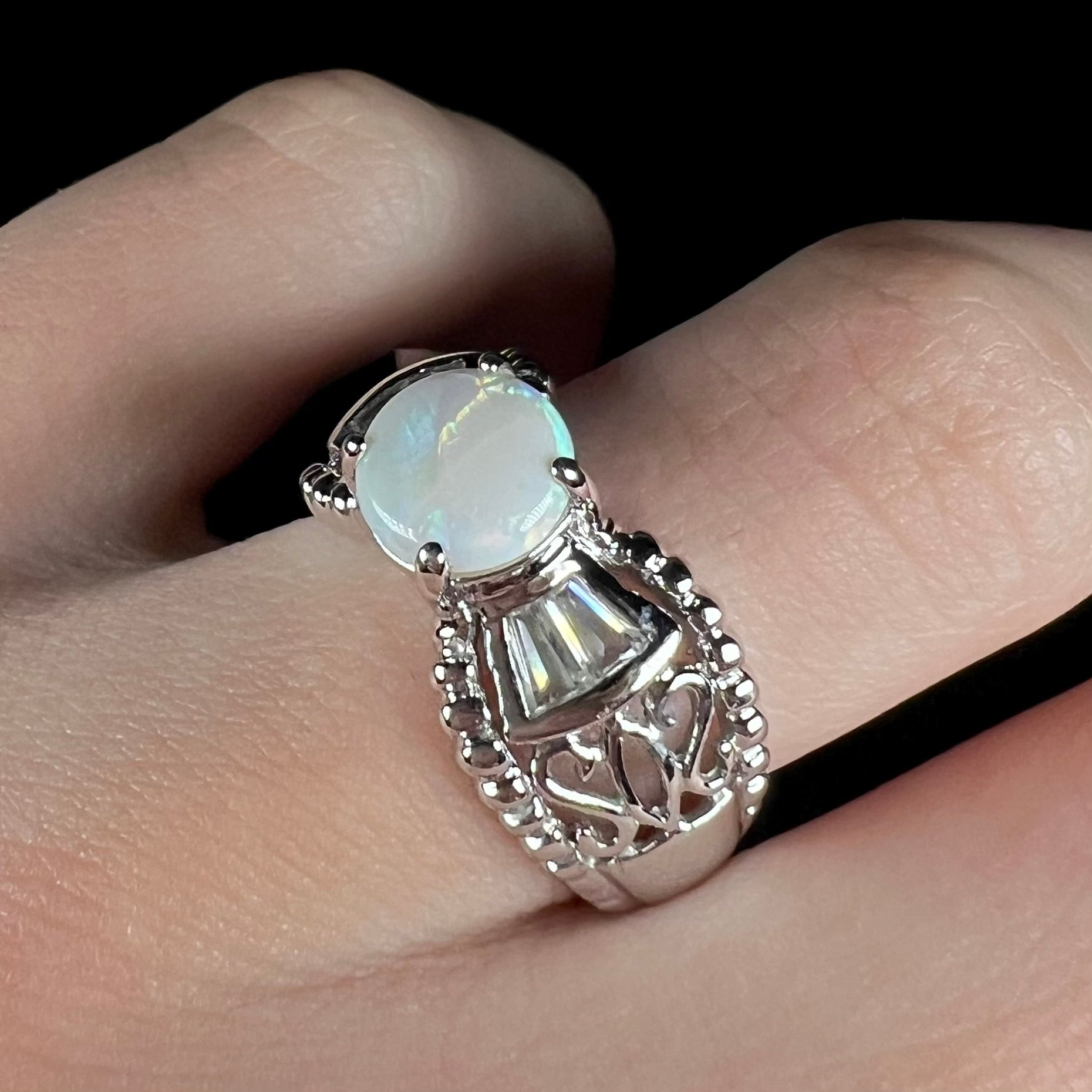 A round Australian white opal and CZ ring in white base metal worn on a finger and viewed at an angle.