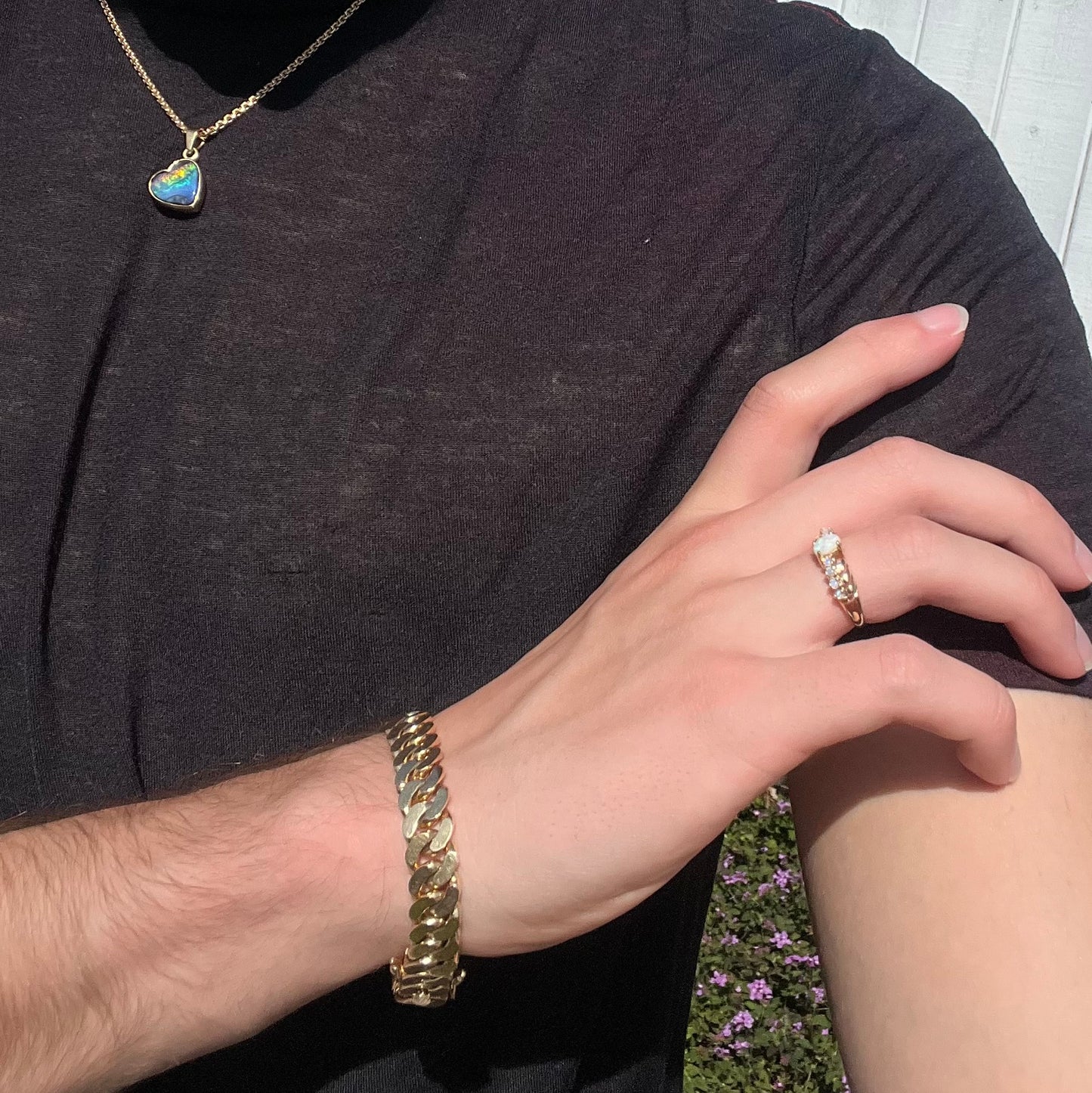 A white opal crisscross ring in yellow gold, worn on a hand that's resting on the model's shoulder in the sunlight.