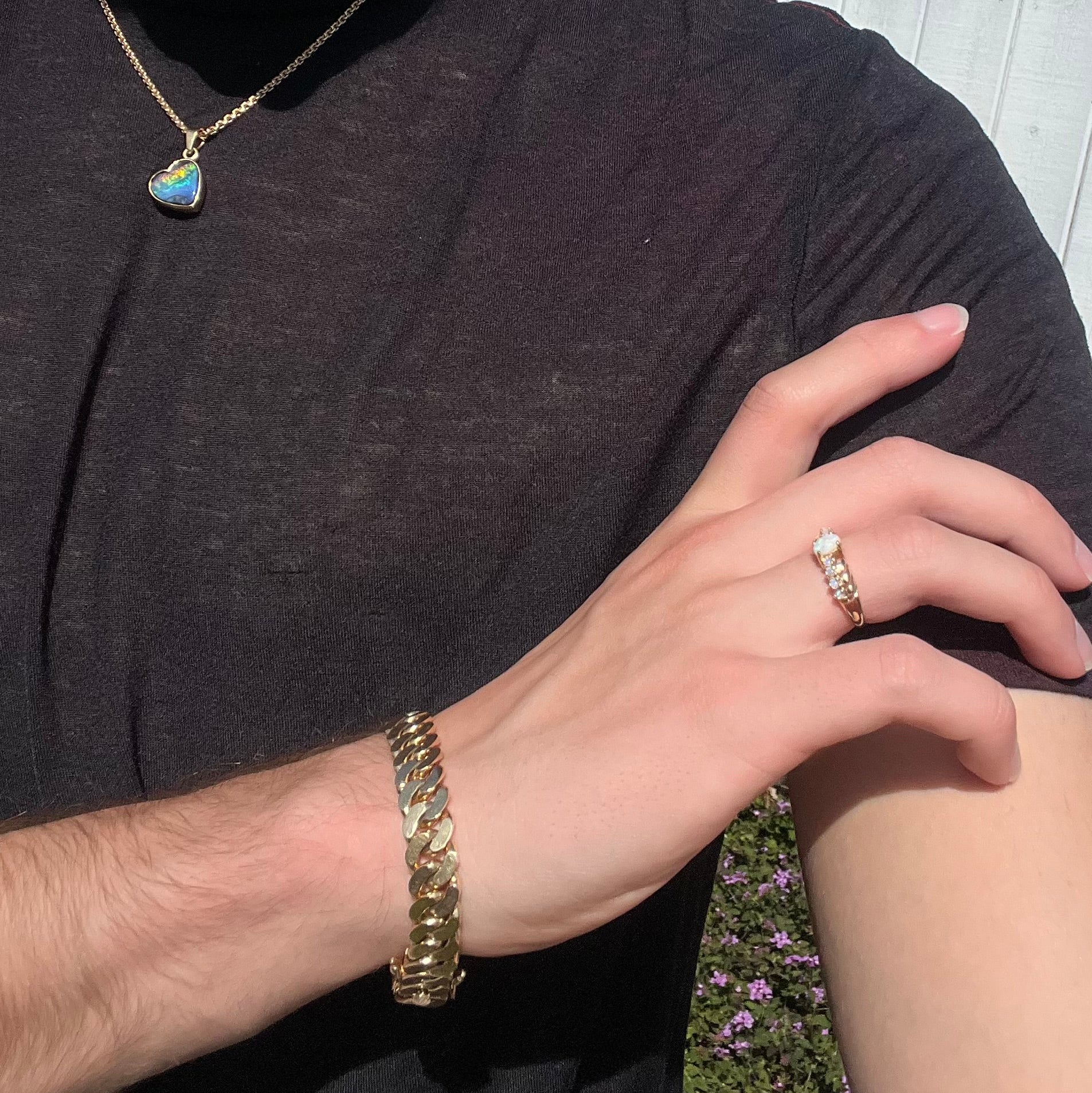 A white opal crisscross ring in yellow gold, worn on a hand that's resting on the model's shoulder in the sunlight.