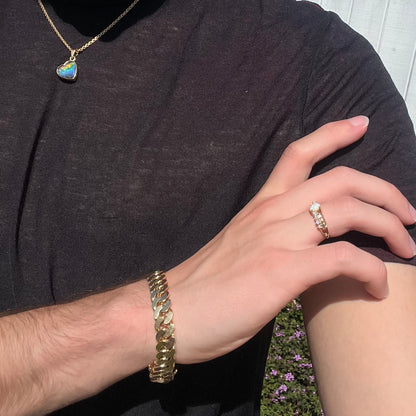 A white opal crisscross ring in yellow gold, worn on a hand that's resting on the model's shoulder in the sunlight.