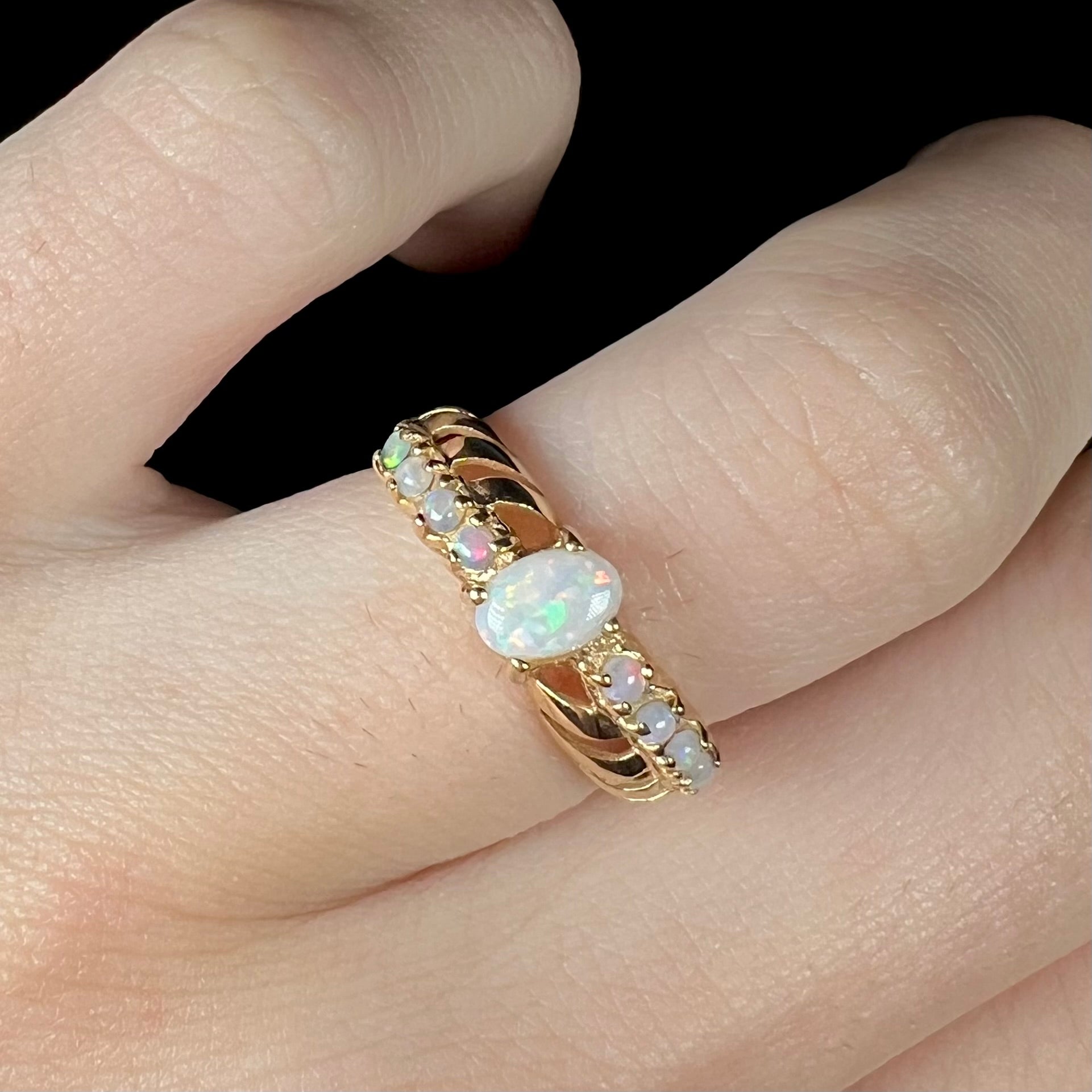 A white opal crisscross ring made from yellow gold, shown close-up on a finger.