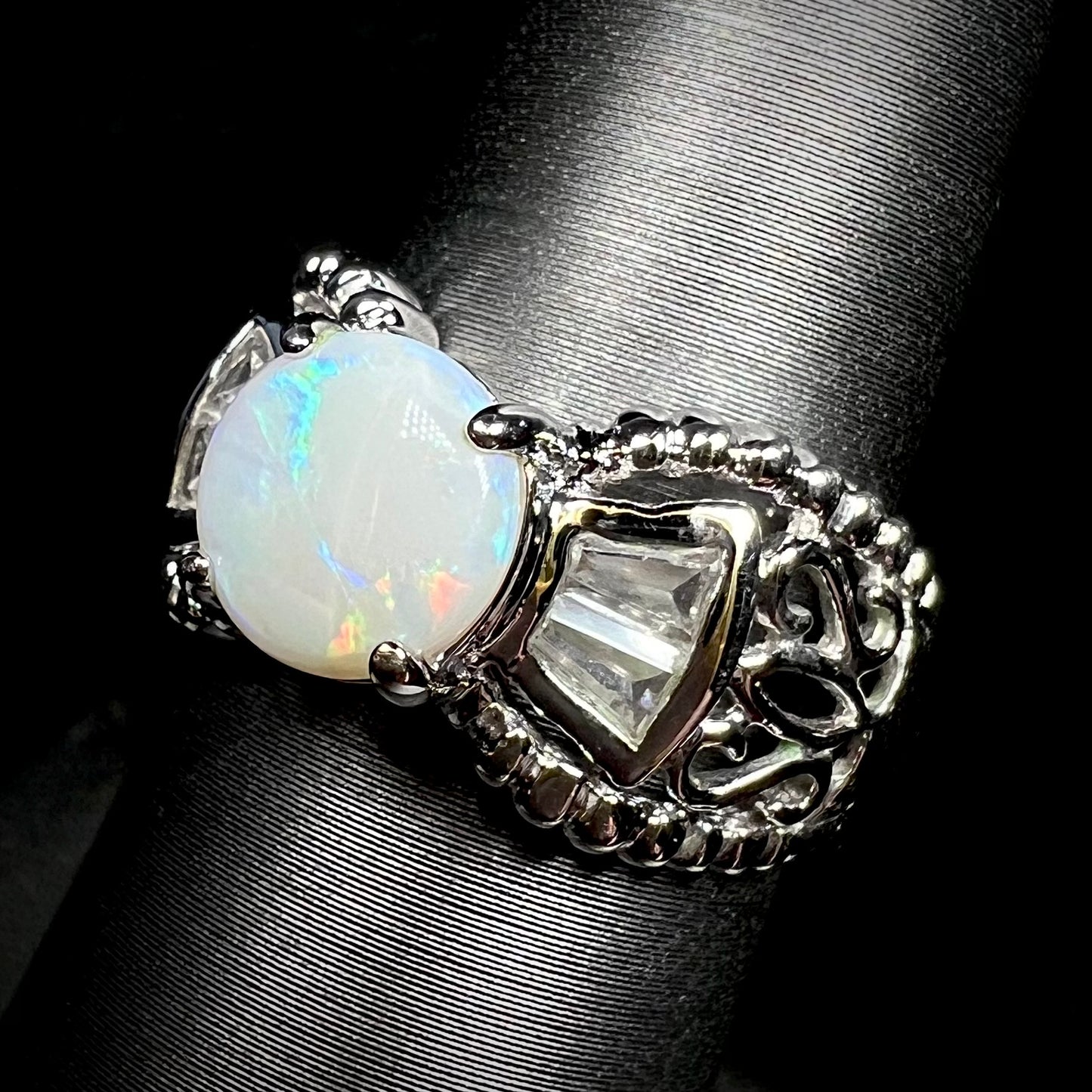 A round Australian white opal and CZ ring in white base metal shown at an angle. 