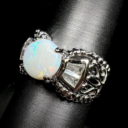 A round Australian white opal and CZ ring in white base metal shown at an angle. 