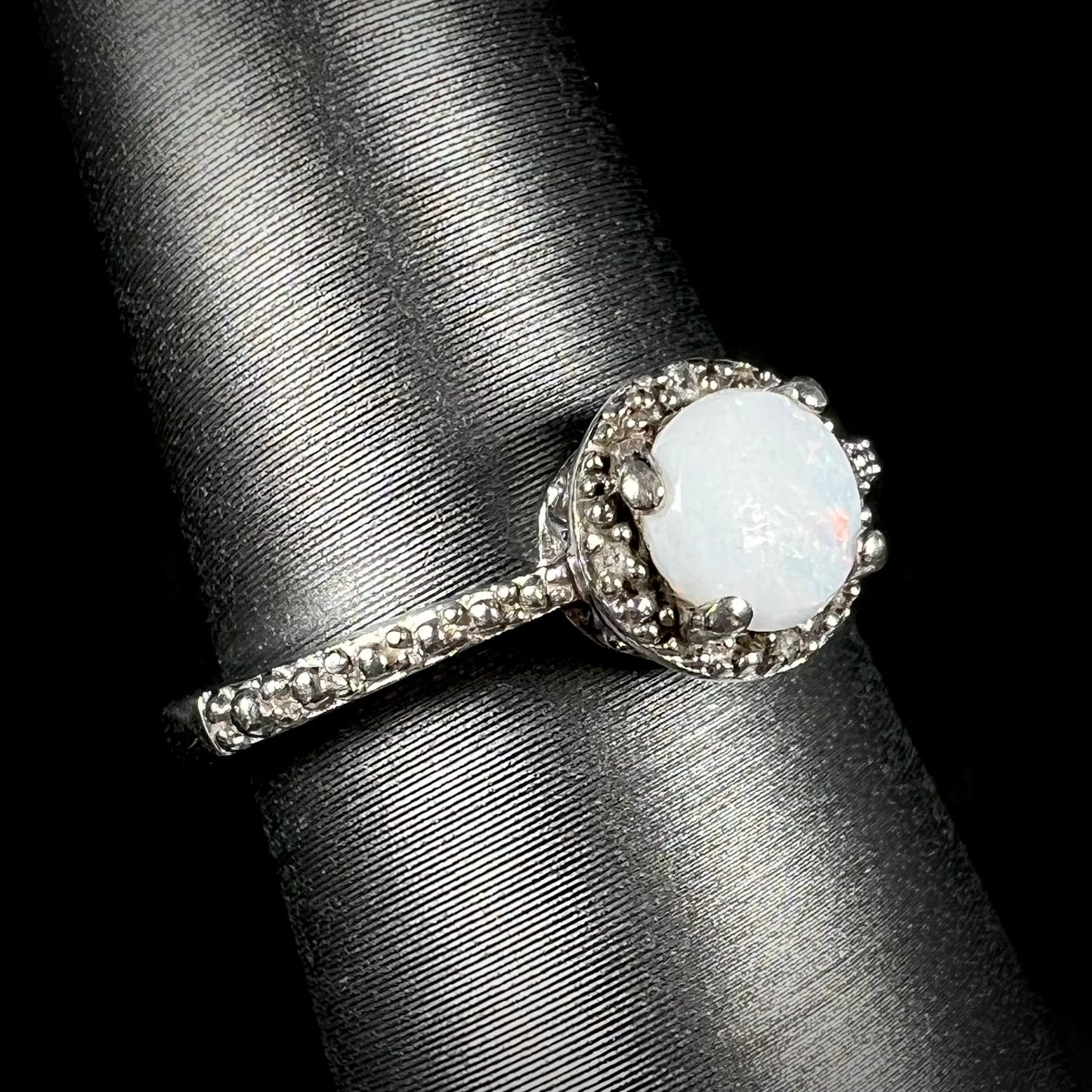 A sterling silver white opal and diamond ring with a halo design shown at an angle.