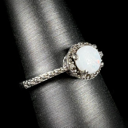 A sterling silver white opal and diamond ring with a halo design shown at an angle.