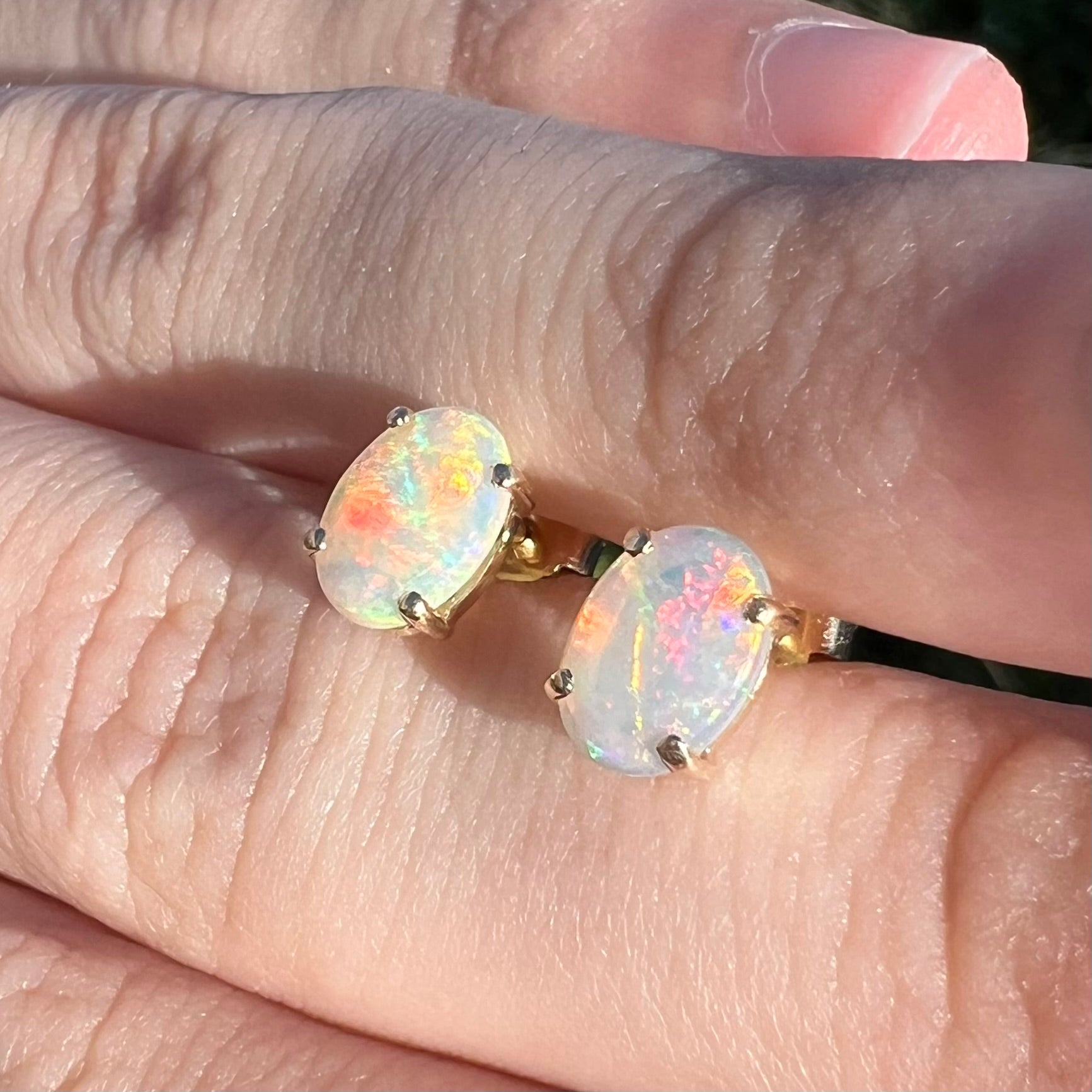 White opal earrings held at an opposing angle, both opals displaying red fire.