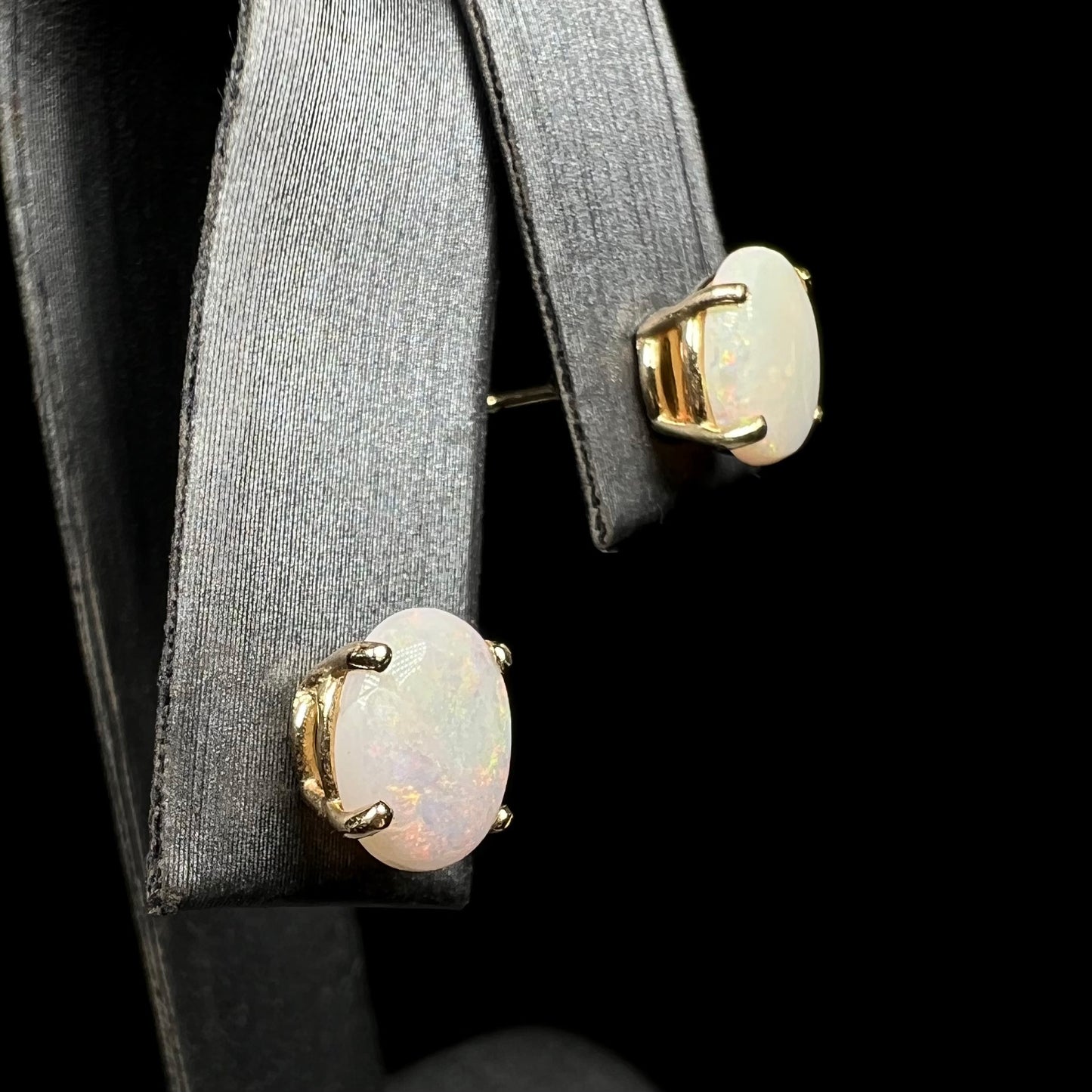 White opal earrings on display, gold settings, angled view