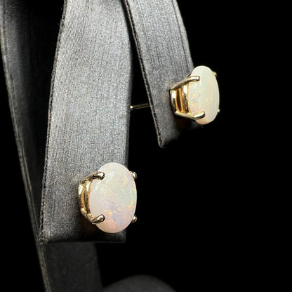 White opal earrings on display, gold settings, angled view