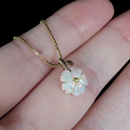 Angled close-up view of a white opal flower pendant held in a hand on a box chain under studio LED lighting.