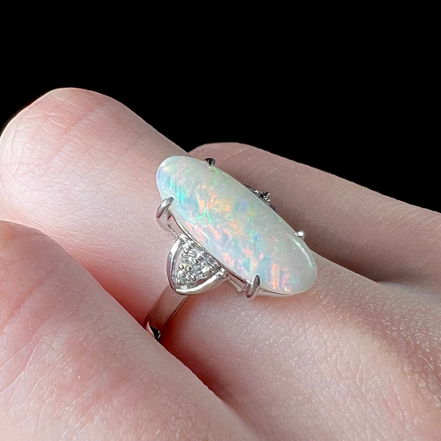 A Coober Pedy white opal platinum ring set with diamond accents.  The opal plays soft pink colors.