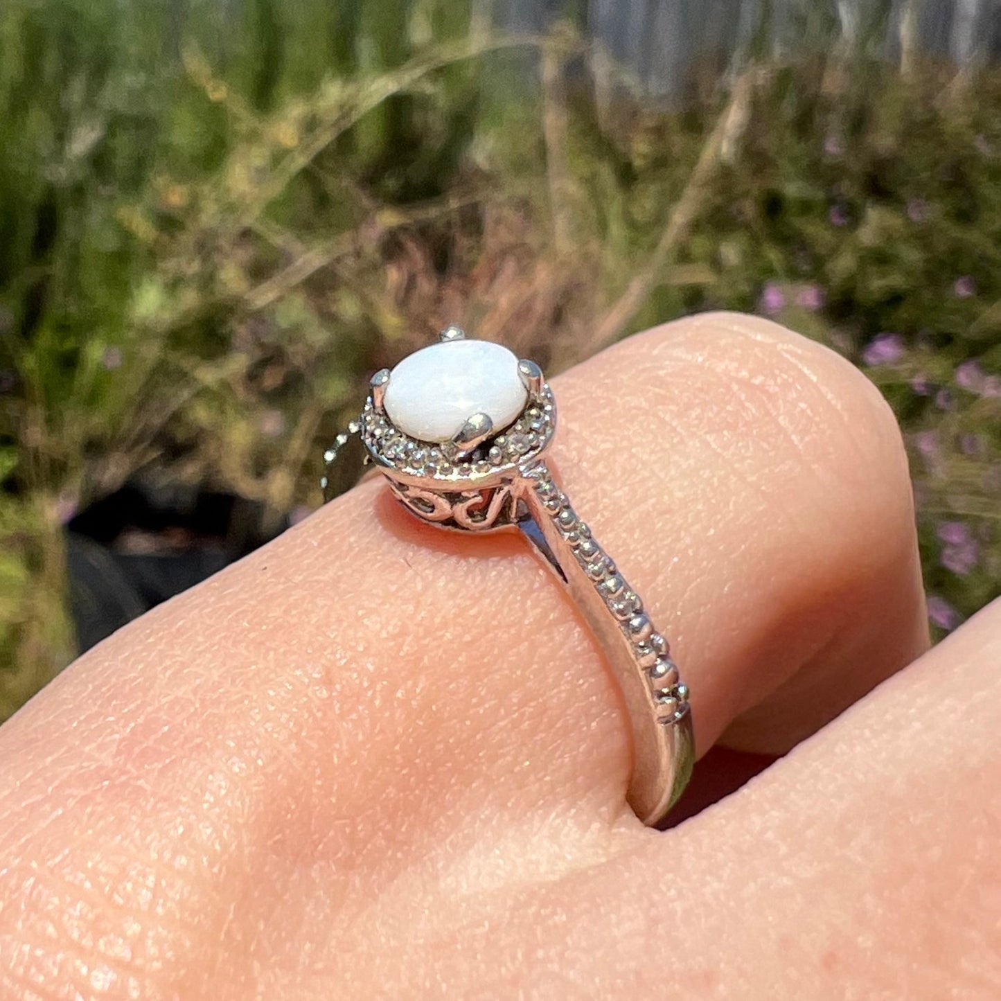A sterling silver white opal ring with diamond accents, shown at an angle worn on a finger in sunlight.