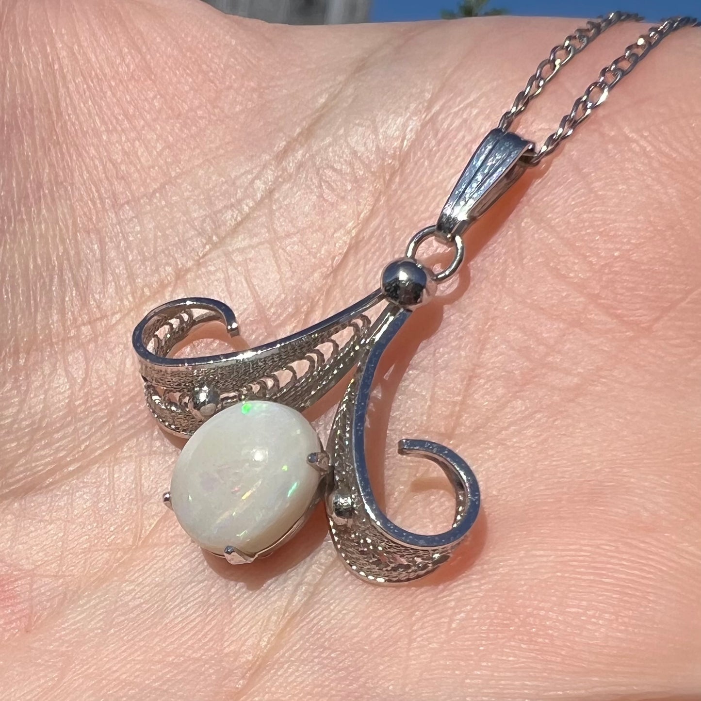 Angled close-up of a Sorrento brand sterling silver Australian white opal pendant shown in sunlight.