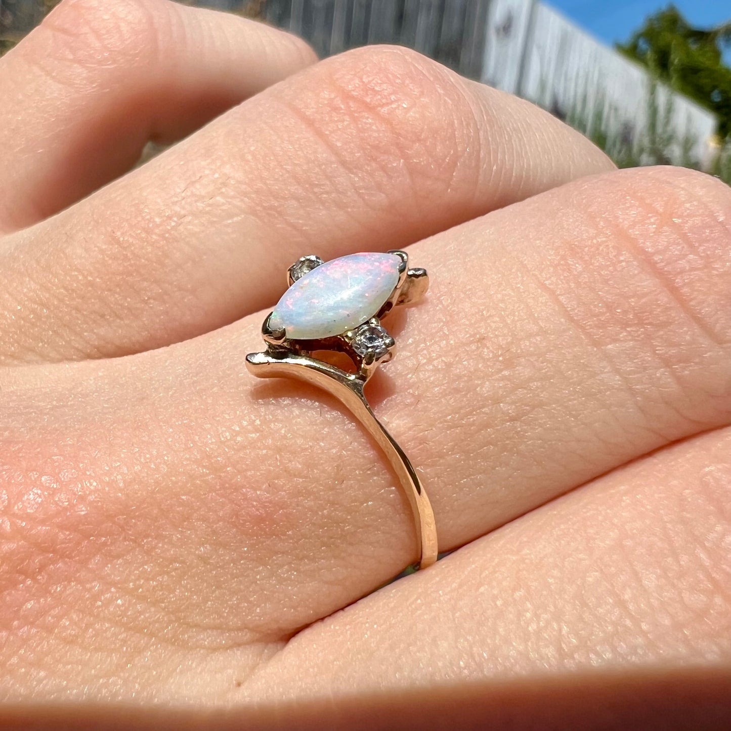 A yellow gold marquise cut opal ring set with two white sapphire accent stones.