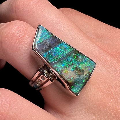 A blue-green Winton boulder opal ring made from platinum, shown at a close-up angle while worn on a finger.