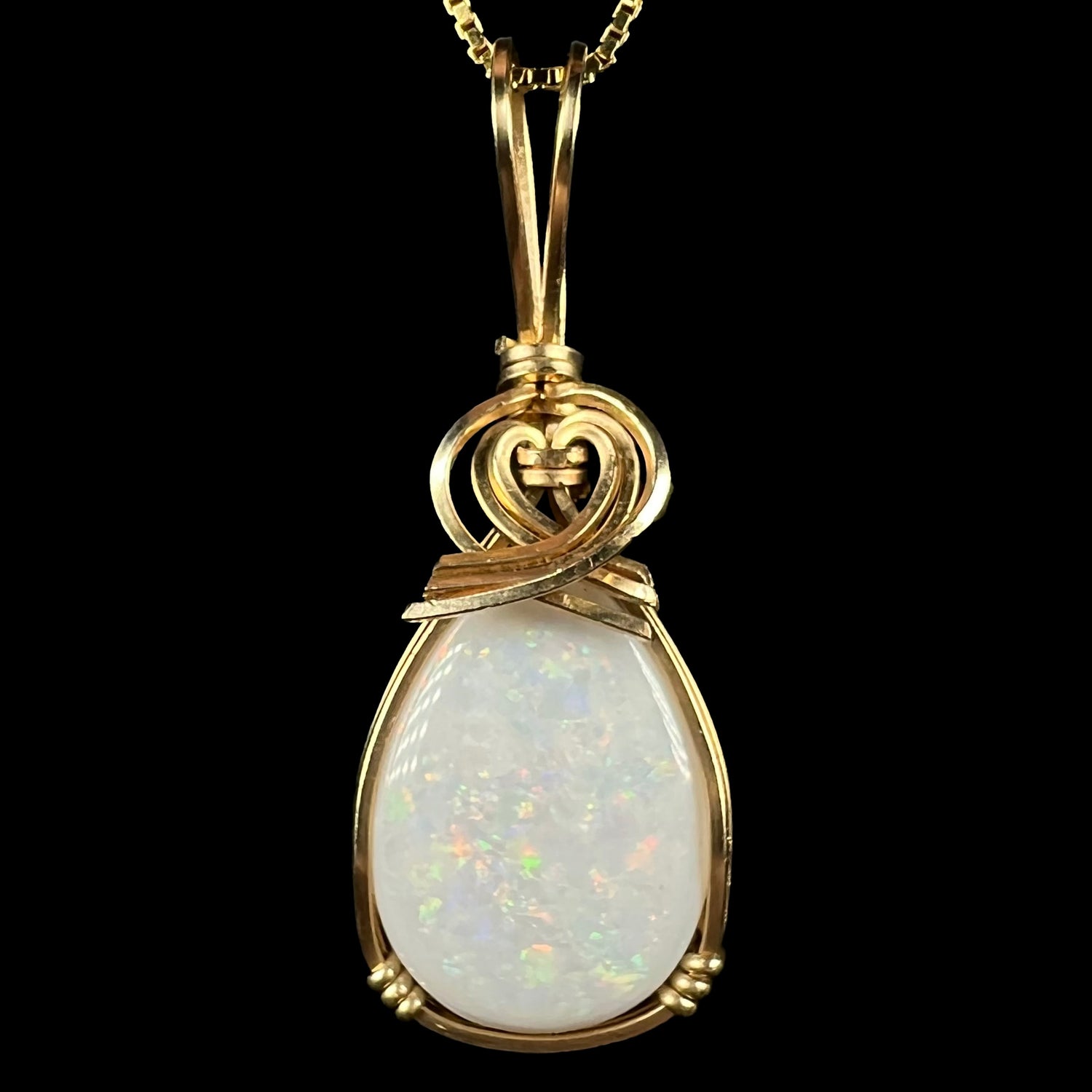 A close-up of a gold wire wrapped opal pendant showing green and red flashes in the stone.