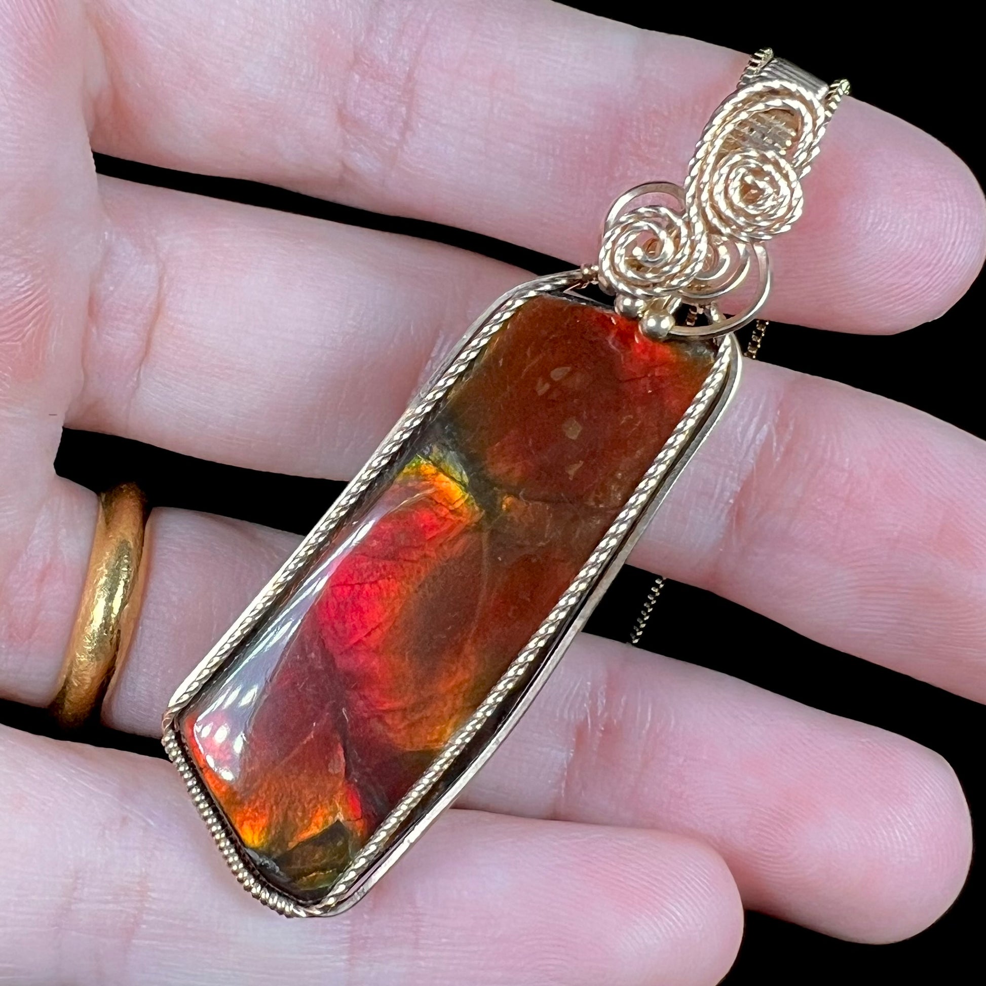 A wire wrapped red ammolite pendant held at an angle by a hand.