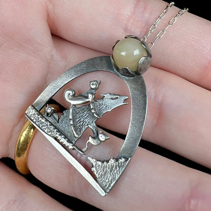 Angled close-up of a sterling silver Ethiopian opal wolf and cat design necklace, shown in a hand.