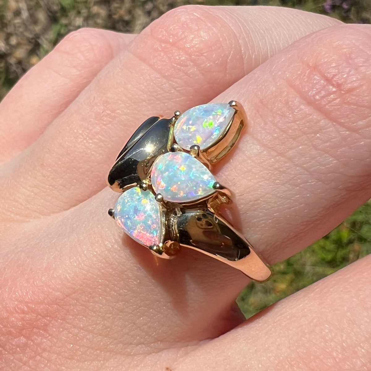 Close-up of hand wearing a women's Modernist-style 14k gold opal ring in the sunlight. The ring has three pear shaped Australian crystal opals.