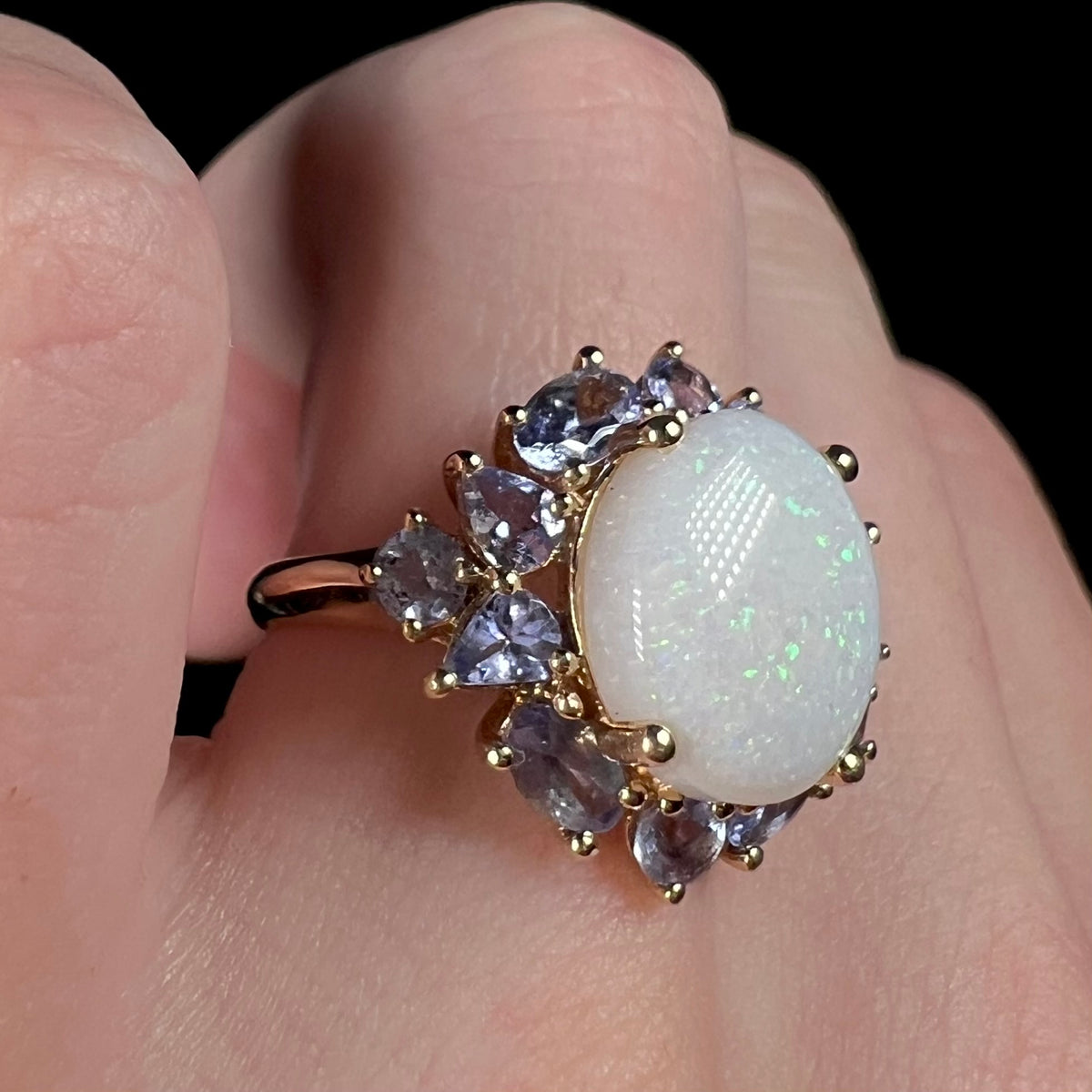 Women's 14k yellow gold Australian opal and tanzanite-accented ring worn on finger, shown close-up from angle