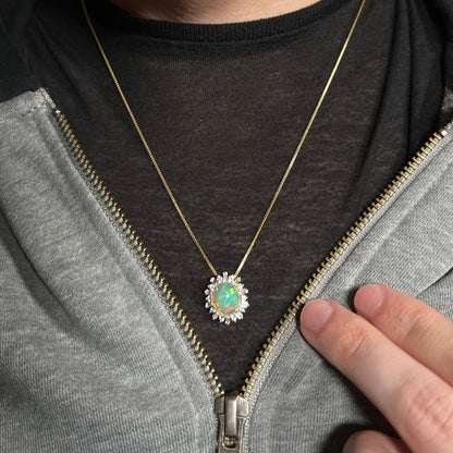 Women's 14k yellow gold Ethiopian fire opal and white sapphire halo necklace worn around person's neck under jacket on dark shirt.