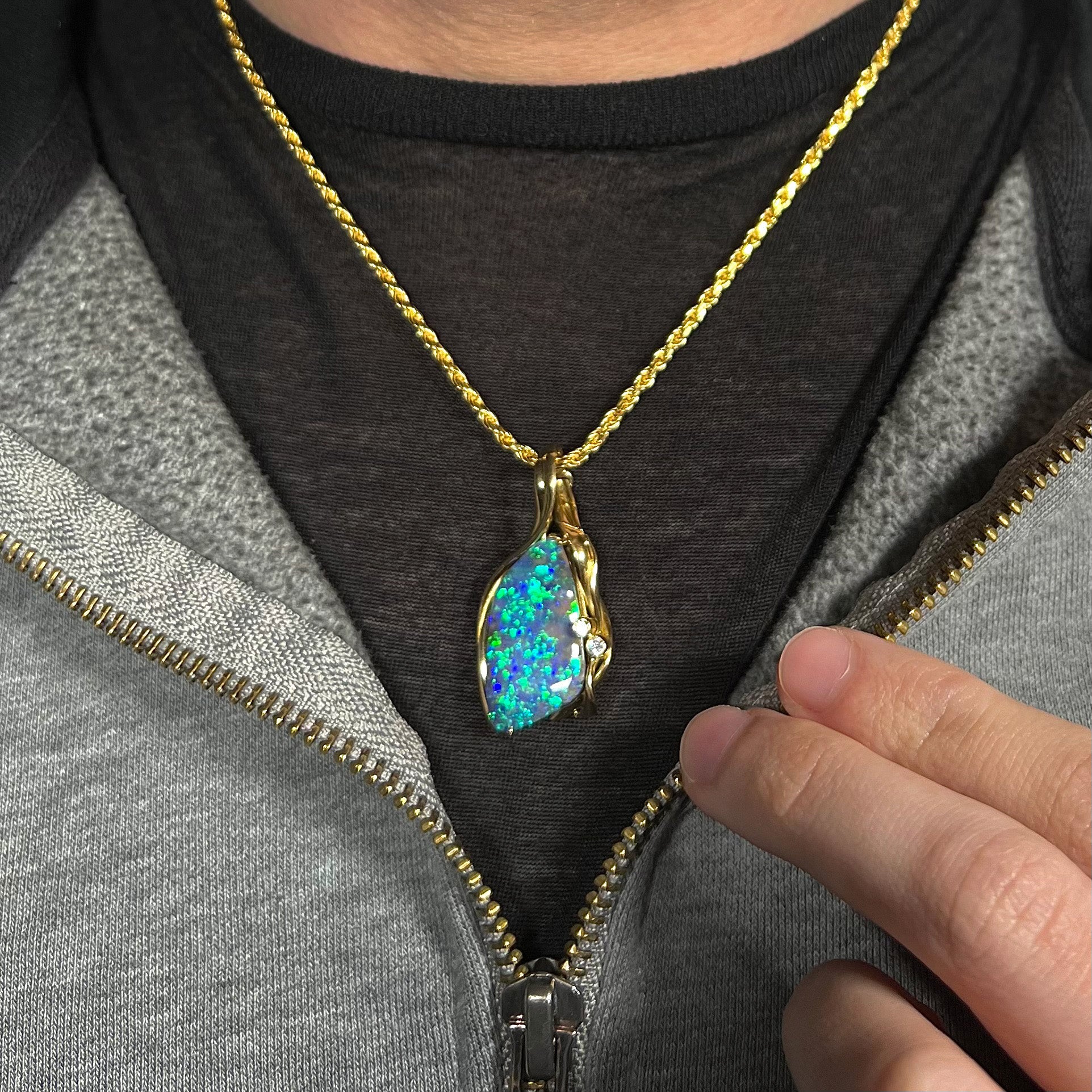 Women's 18k gold Australian boulder opal necklace with bright green and blue fire worn around model's neck with gray jacket.