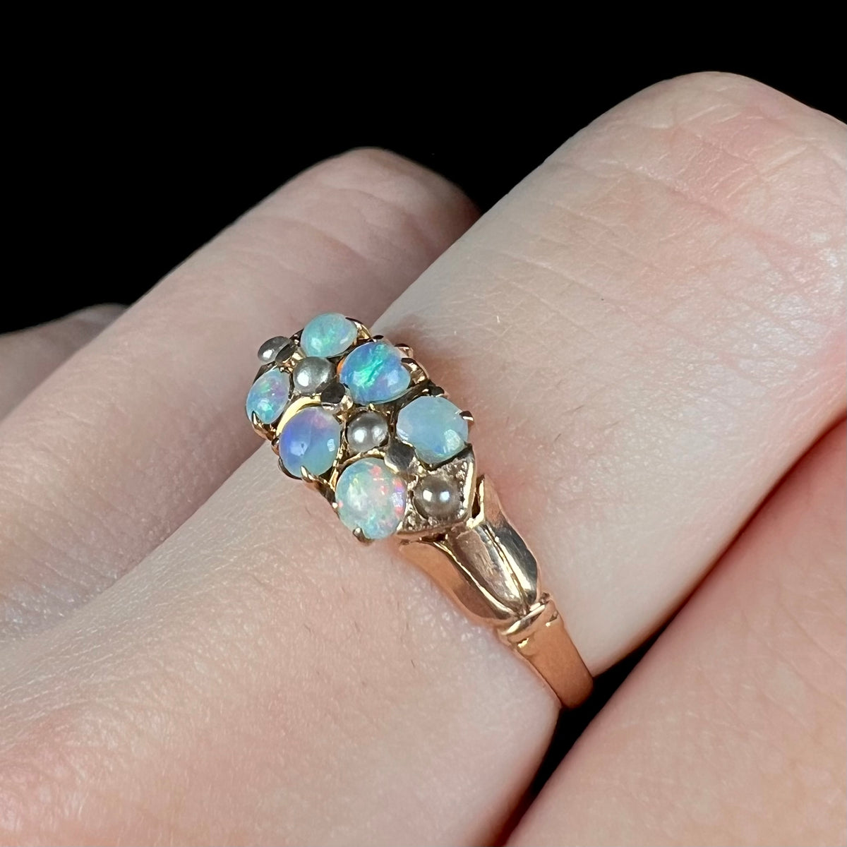 Angled close-up of women's 9k gold opal and pearl ring, worn on finger under LED studio light