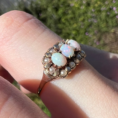 Finger wearing a women's antique Australian opal ring with seed pearl accents in sunlight, shown close-up from angle