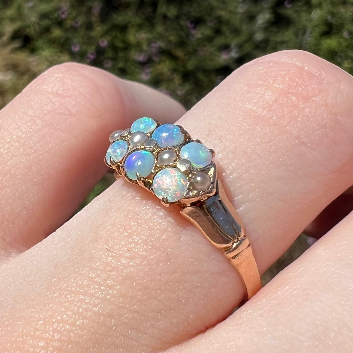 Angled close-up of women's antique gold opal and pearl ring, worn on finger and viewed from angle in sunlight