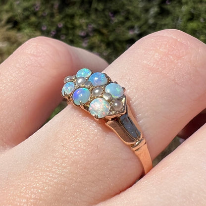 Angled close-up of women's antique gold opal and pearl ring, worn on finger and viewed from angle in sunlight