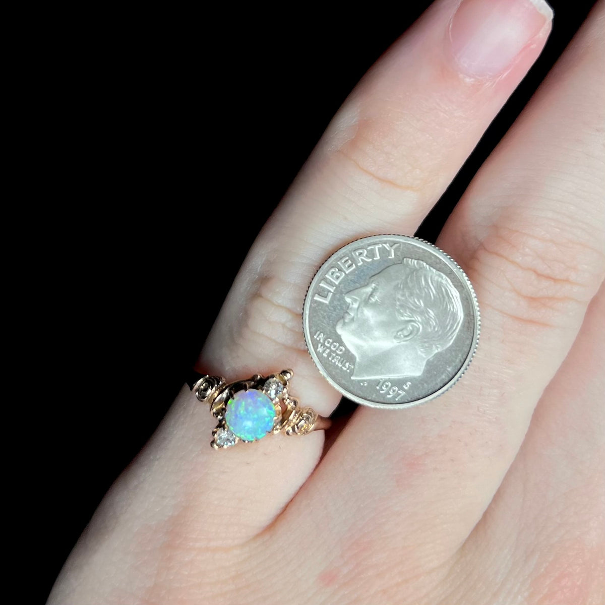 Women's antique three-stone opal and diamond ring from Art Nouveau era worn on pinky finger next to US dime coin for scale