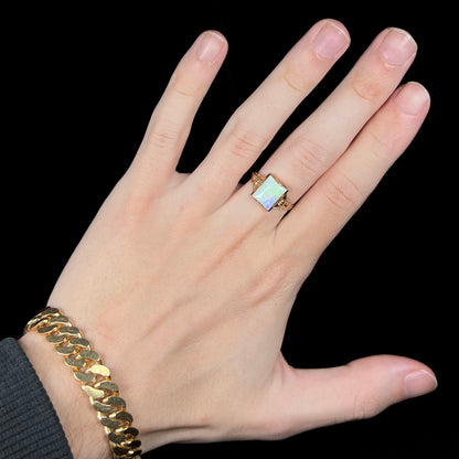 Hand wearing a women's antique Art Deco solitaire ring set with a rectangle cut opal in 10k yellow gold on middle finger