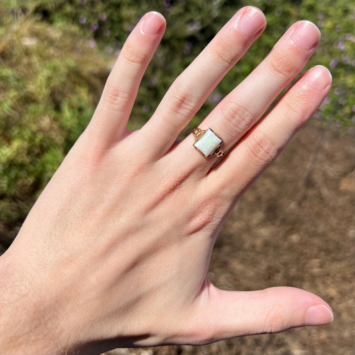 Hand wearing a women's Art Deco solitaire opal ring in 10k gold under natural sunlight