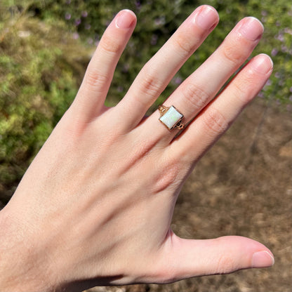 Hand wearing a women's Art Deco solitaire opal ring in 10k gold under natural sunlight