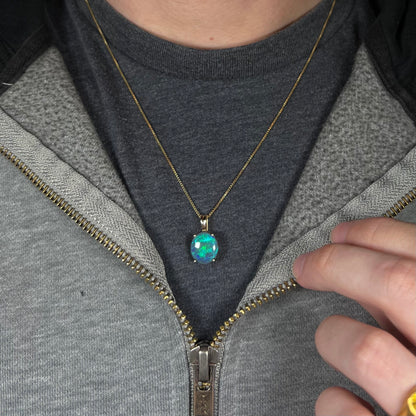 Women's Australian black opal necklace with blue and green colors in 14k gold, worn around person's neck