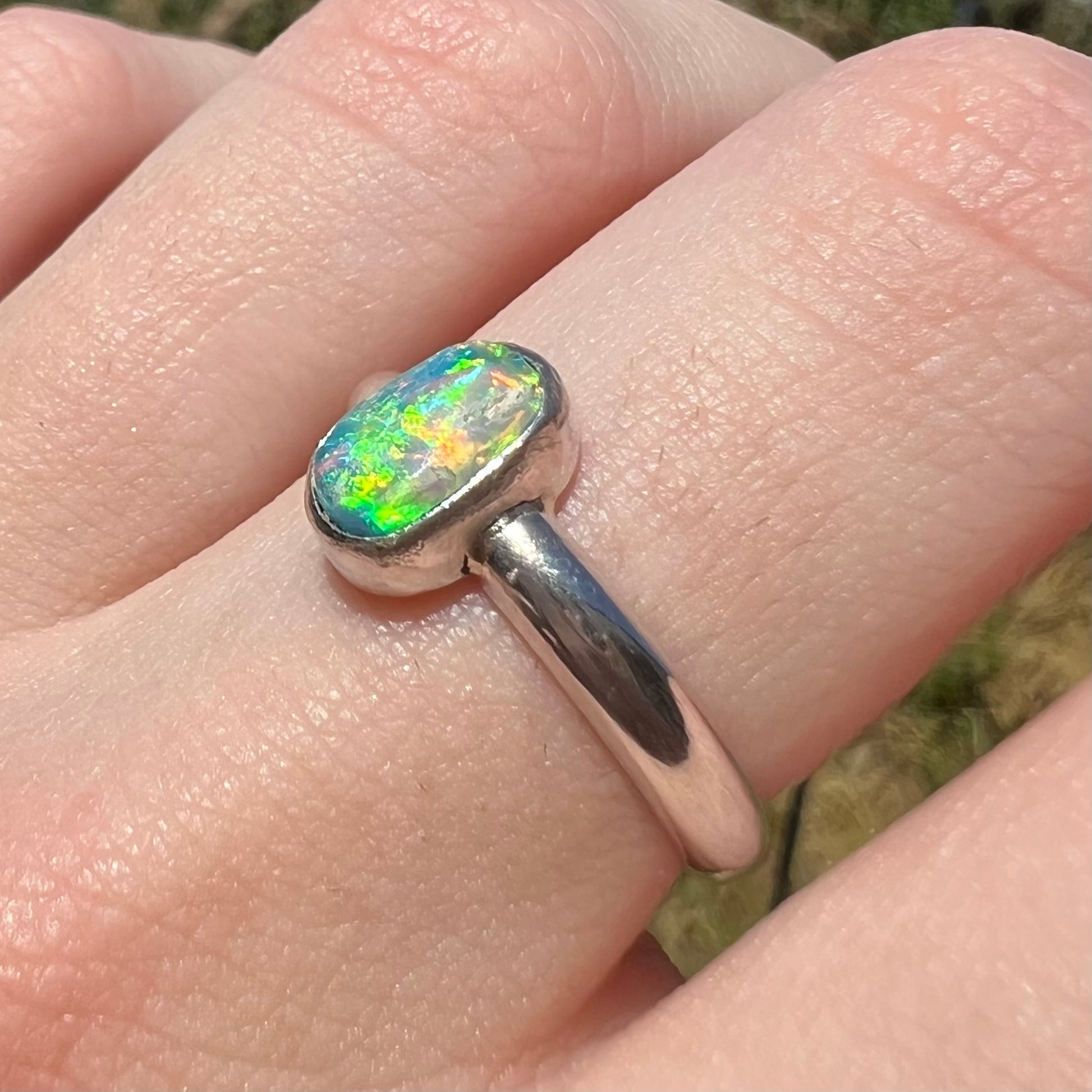 Women's silver Australian crystal opal ring showing green and orange flashes in natural light, worn on finger