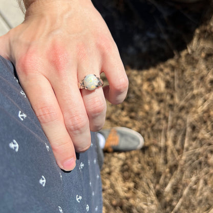 Person's sunlit hand resting on hip wearing a women's Australian opal solitaire ring with textured white gold prong-set design