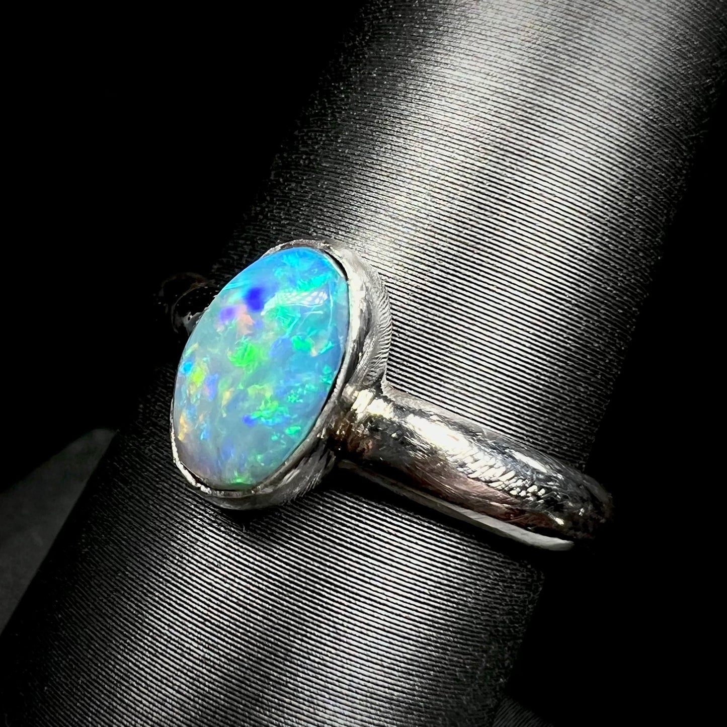 Angled macro view of a women's Australian opal ring in sterling silver, shown on a ring display.  The opal has green and blue colors over a blue body.