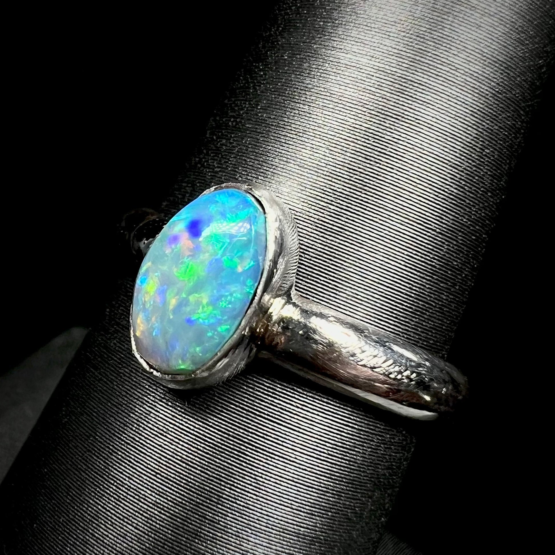 Angled macro view of a women's Australian opal ring in sterling silver, shown on a ring display.  The opal has green and blue colors over a blue body.