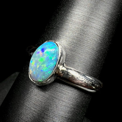 Angled macro view of a women's Australian opal ring in sterling silver, shown on a ring display.  The opal has green and blue colors over a blue body.