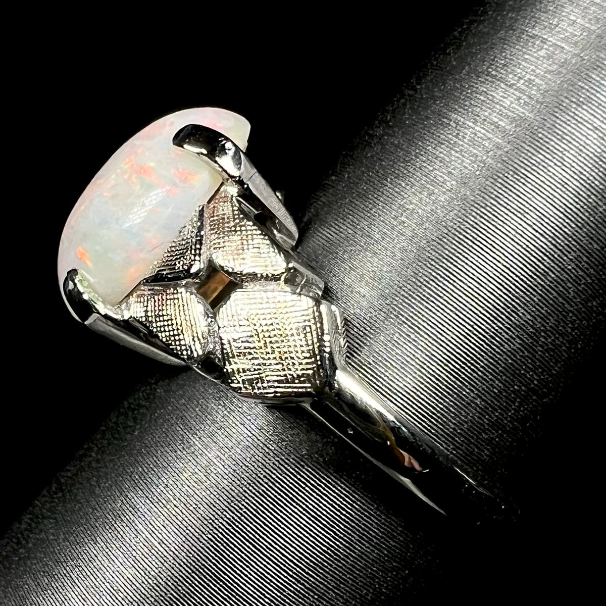 Side view of an Australian opal women's ring in 14k white gold, shown on ring display; the ring's shank and textured shoulders are in focus