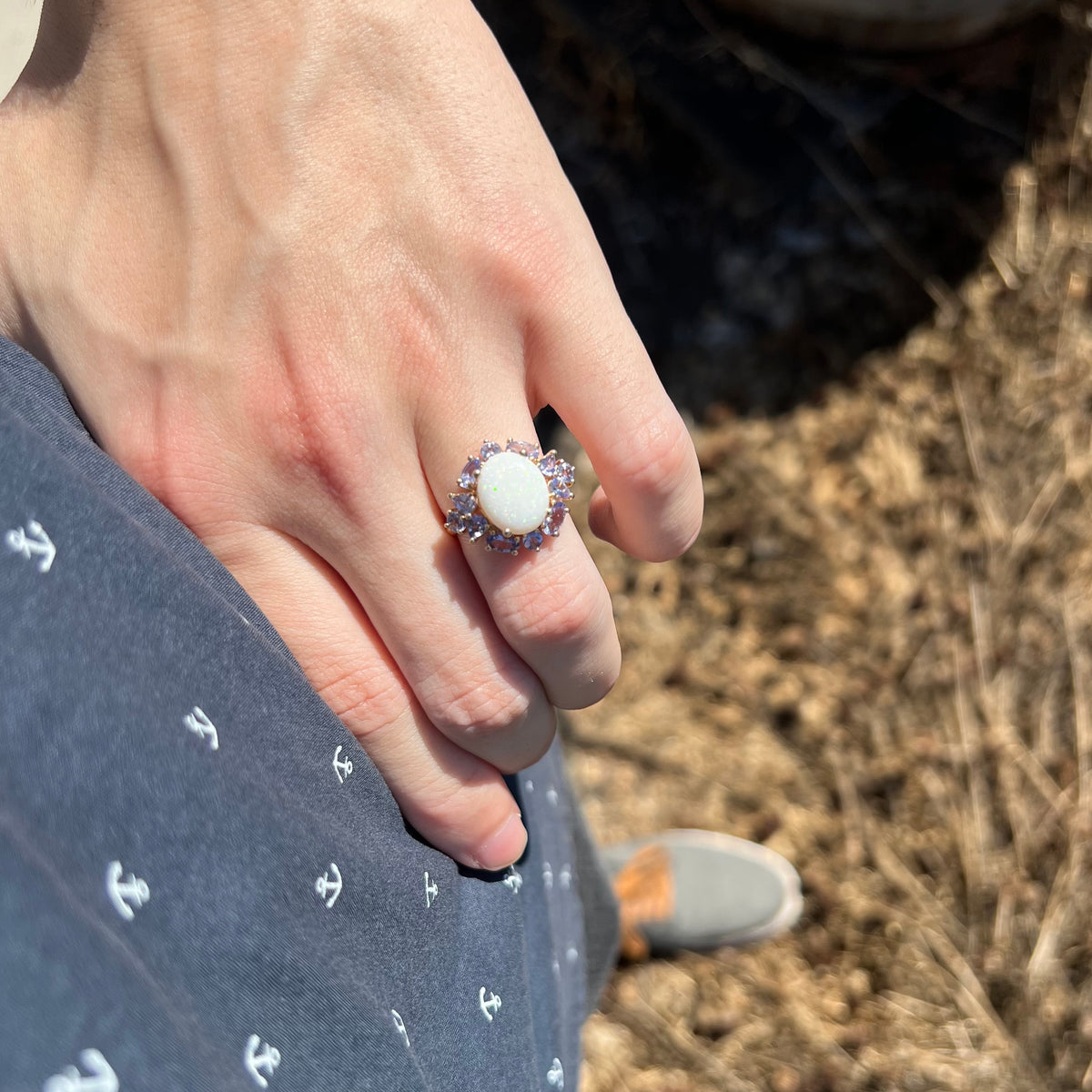 Person's hand resting on hip in sunlight wearing women's 14k gold Australian opal and tanzanite ring