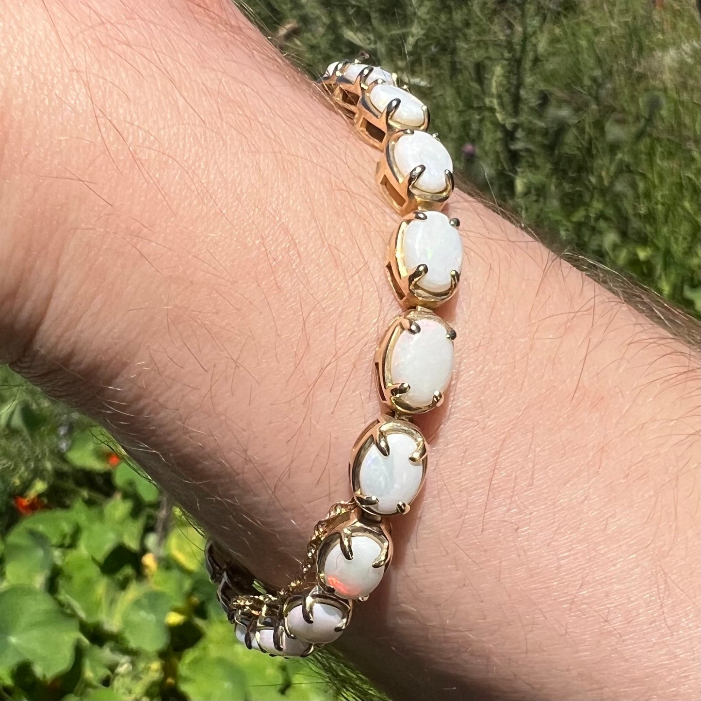 Close-up of women's yellow gold Australian opal tennis bracelet worn around wrist in natural light.