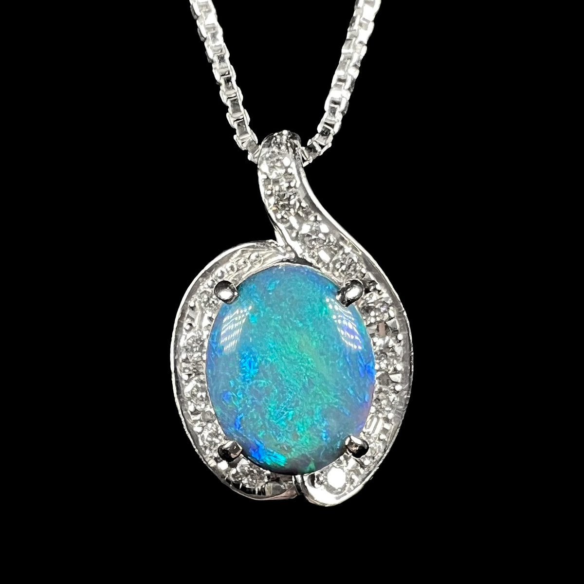 Close-up view of women's black opal and diamond pendant with asymmetrical halo design, shown on silver chain against black background.