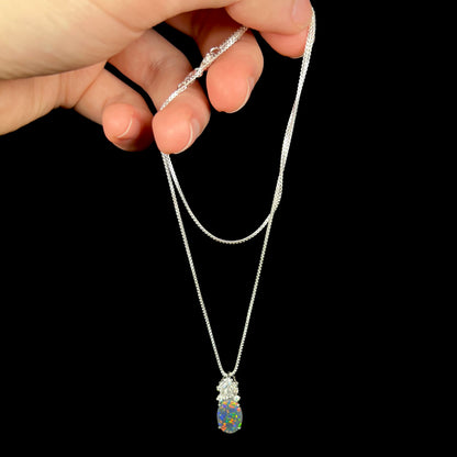 Hand dangling women's platinum black opal pineapple necklace with diamond crown from silver chain.
