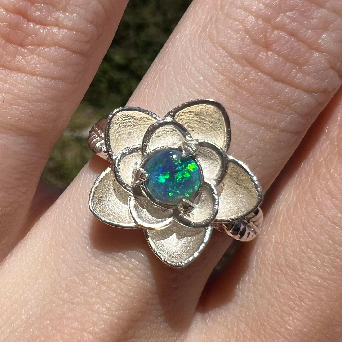 Close-up of women's black opal ring with sterling silver lotus flower motif, worn on finger in sunlight